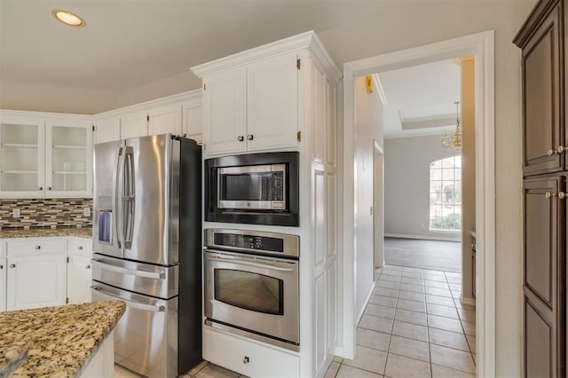 kitchen featuring light tile patterned floors, white cabinetry, stainless steel appliances, light stone countertops, and decorative backsplash