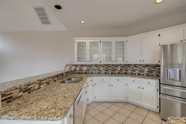 kitchen with appliances with stainless steel finishes, white cabinetry, sink, light tile patterned floors, and light stone counters