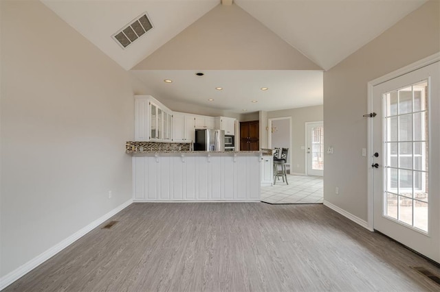 unfurnished living room with vaulted ceiling, plenty of natural light, and light wood-type flooring