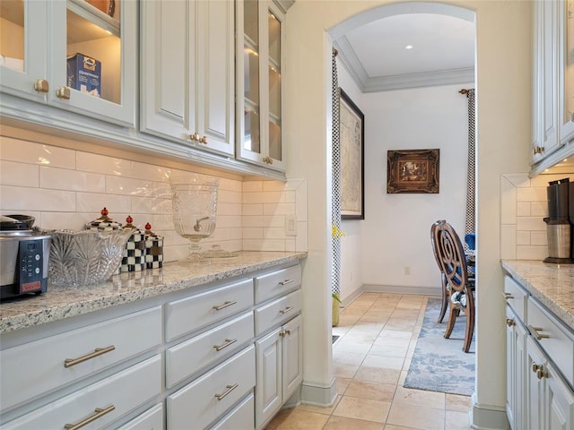 5808 Mistletoe Ct, Oklahoma City, OK 73142 - kitchen with white cabinetry, tasteful backsplash, light stone counters, light tile patterned floors, and ornamental molding