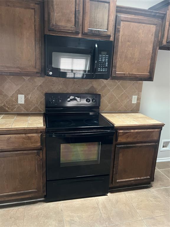 kitchen featuring black appliances, dark brown cabinets, and tile counters