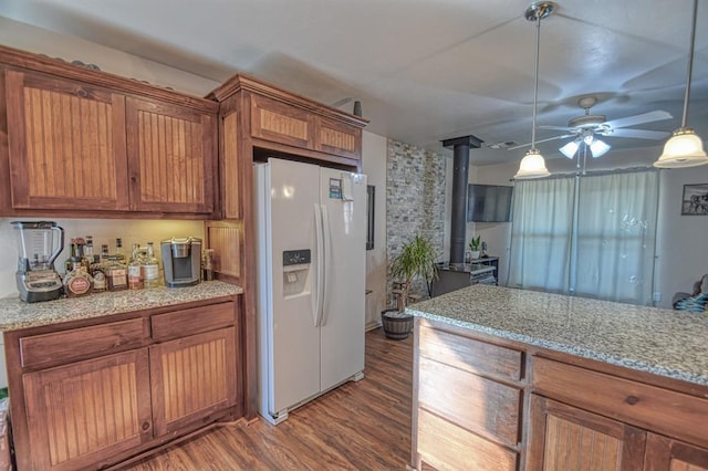 kitchen with light stone counters, wood-type flooring, a wood stove, white fridge with ice dispenser, and pendant lighting