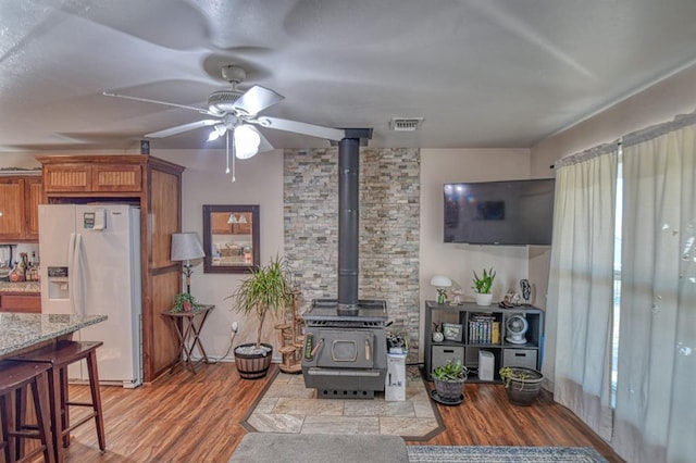 living room with ceiling fan, a wood stove, and light hardwood / wood-style floors