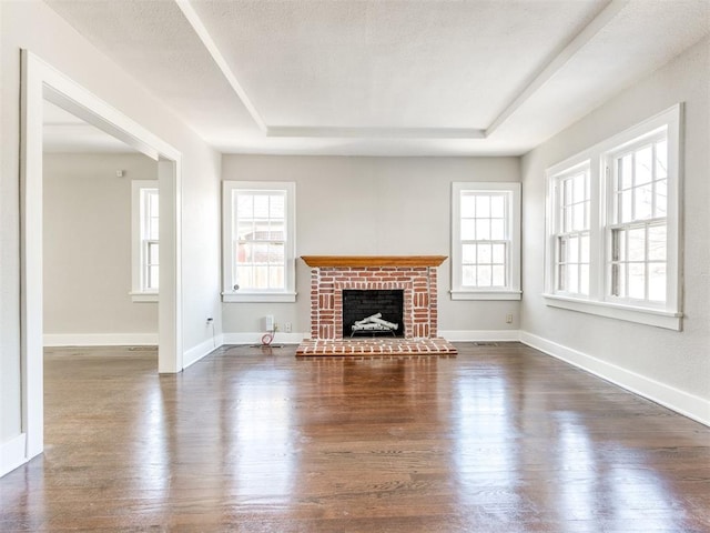 unfurnished living room featuring a brick fireplace, a textured ceiling, dark hardwood / wood-style flooring, and a tray ceiling