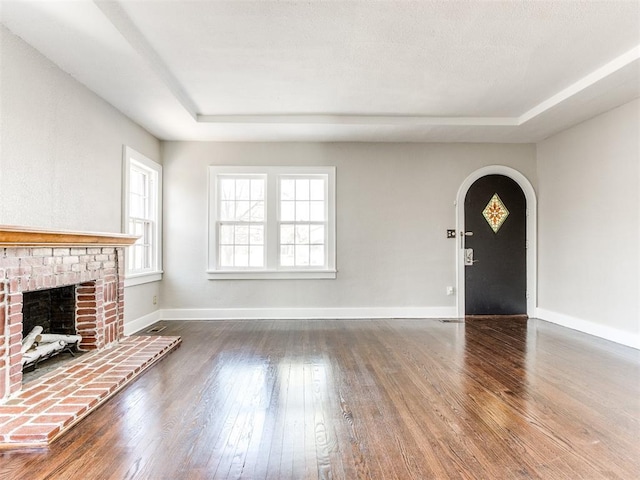 unfurnished living room featuring hardwood / wood-style floors, a raised ceiling, and a brick fireplace