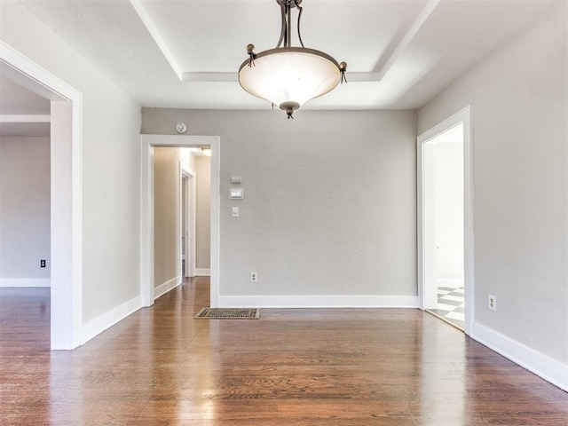 empty room featuring a raised ceiling and dark hardwood / wood-style floors