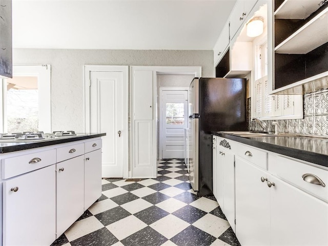 kitchen with stainless steel refrigerator, tasteful backsplash, white cabinetry, sink, and gas stovetop