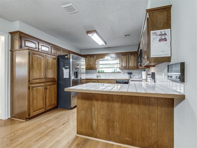 kitchen featuring kitchen peninsula, appliances with stainless steel finishes, a textured ceiling, light hardwood / wood-style flooring, and tile counters