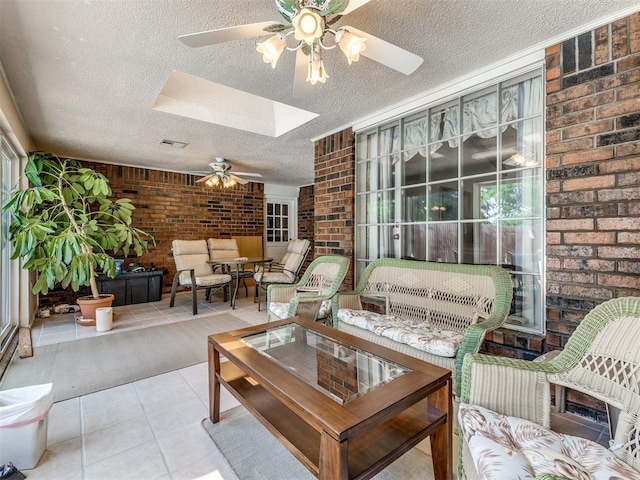 interior space featuring a skylight, ceiling fan, light tile patterned floors, a textured ceiling, and brick wall