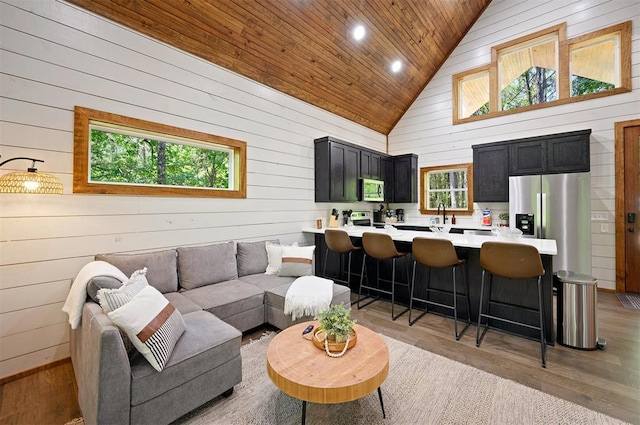 living room featuring wood ceiling, wood walls, light wood-type flooring, a healthy amount of sunlight, and high vaulted ceiling