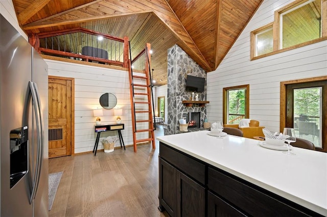 kitchen with wooden walls, a fireplace, wooden ceiling, and stainless steel fridge