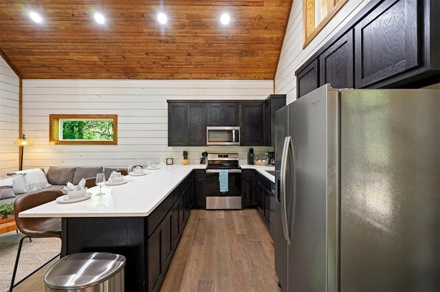 kitchen featuring wooden walls, a kitchen bar, light wood-type flooring, wood ceiling, and appliances with stainless steel finishes