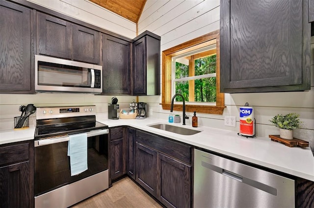 kitchen featuring wood walls, appliances with stainless steel finishes, dark brown cabinetry, sink, and lofted ceiling