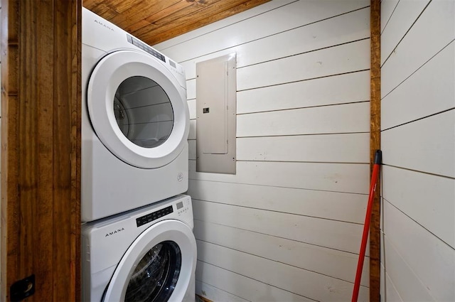 laundry area with electric panel, wooden walls, stacked washer / dryer, and wooden ceiling