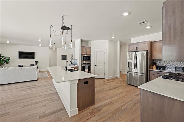 kitchen featuring sink, decorative light fixtures, decorative backsplash, a center island with sink, and appliances with stainless steel finishes