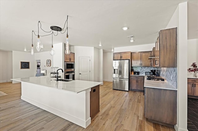 kitchen featuring sink, hanging light fixtures, light stone counters, backsplash, and appliances with stainless steel finishes