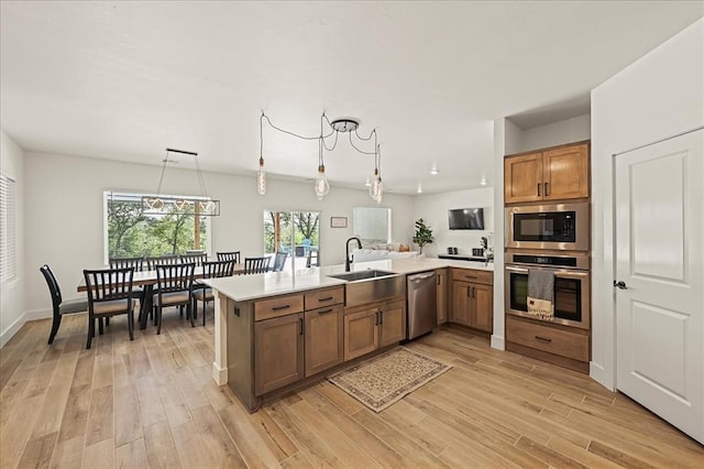 kitchen featuring kitchen peninsula, appliances with stainless steel finishes, sink, light hardwood / wood-style floors, and hanging light fixtures