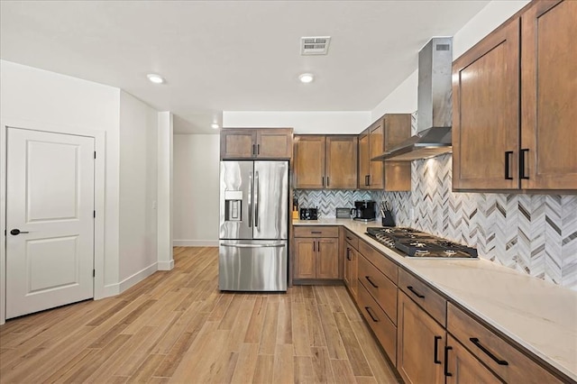 kitchen with tasteful backsplash, stainless steel appliances, wall chimney range hood, and light wood-type flooring