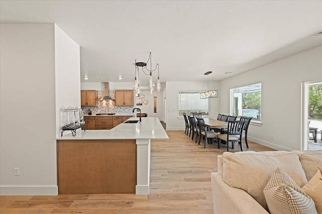 kitchen featuring sink, hanging light fixtures, wall chimney range hood, kitchen peninsula, and light wood-type flooring