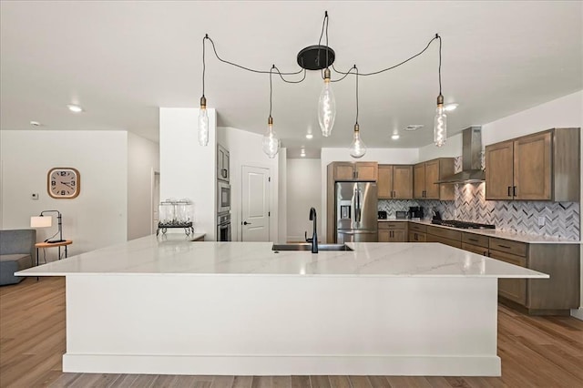 kitchen with appliances with stainless steel finishes, backsplash, sink, wall chimney range hood, and light hardwood / wood-style floors