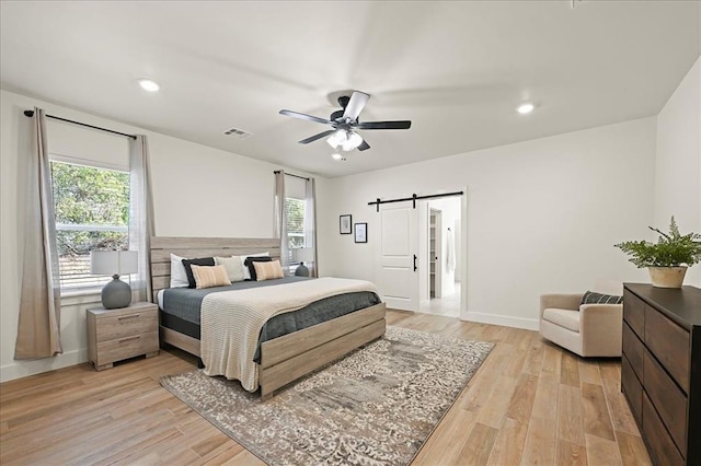 bedroom with light wood-type flooring, a barn door, and ceiling fan