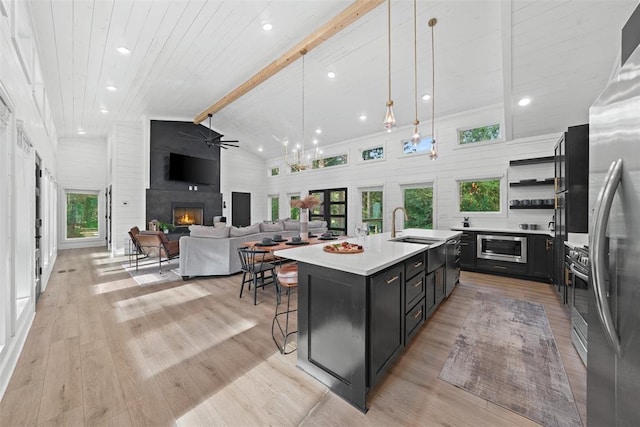 kitchen with beamed ceiling, decorative light fixtures, light wood-type flooring, and a kitchen island with sink