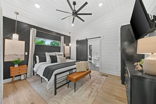 bedroom featuring a barn door, ceiling fan, light hardwood / wood-style flooring, and vaulted ceiling