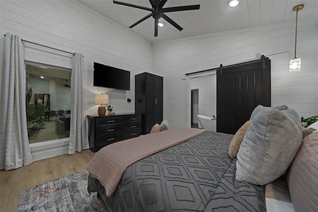 bedroom with wooden walls, vaulted ceiling, ceiling fan, a barn door, and light wood-type flooring