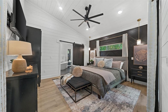 bedroom featuring light wood-type flooring, vaulted ceiling, ceiling fan, wooden walls, and a barn door