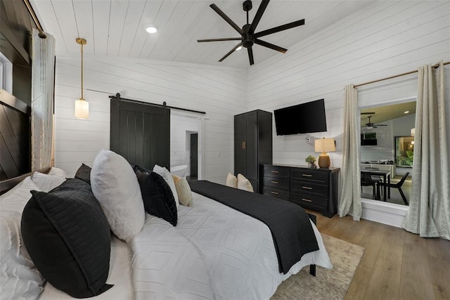 bedroom featuring a barn door, wooden walls, vaulted ceiling, and light wood-type flooring