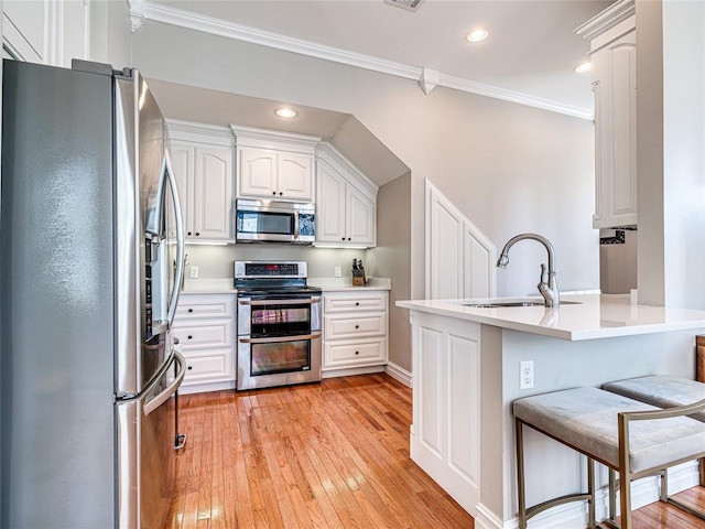 kitchen featuring appliances with stainless steel finishes, white cabinets, light countertops, and a kitchen breakfast bar