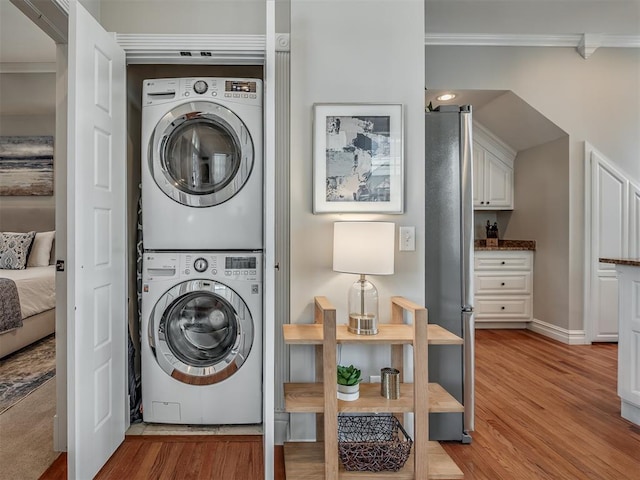 laundry area with laundry area, ornamental molding, light wood-style floors, and stacked washer and clothes dryer