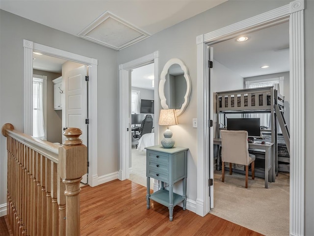 hallway featuring baseboards, light wood-style flooring, an upstairs landing, and attic access