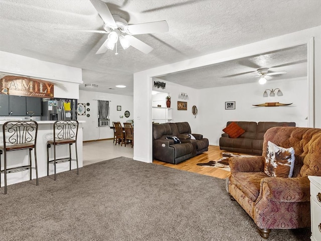 living room featuring light carpet, a textured ceiling, and ceiling fan