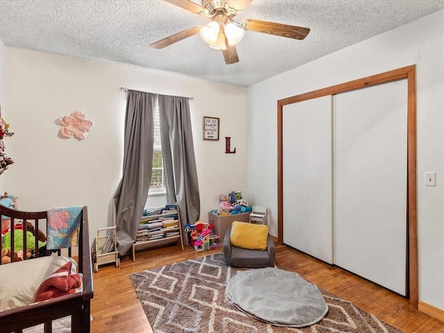 bedroom featuring a textured ceiling, light wood-type flooring, a closet, and ceiling fan