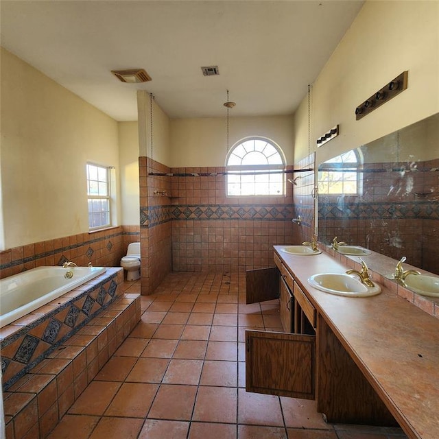 bathroom with tile patterned flooring, a relaxing tiled tub, toilet, vanity, and tile walls