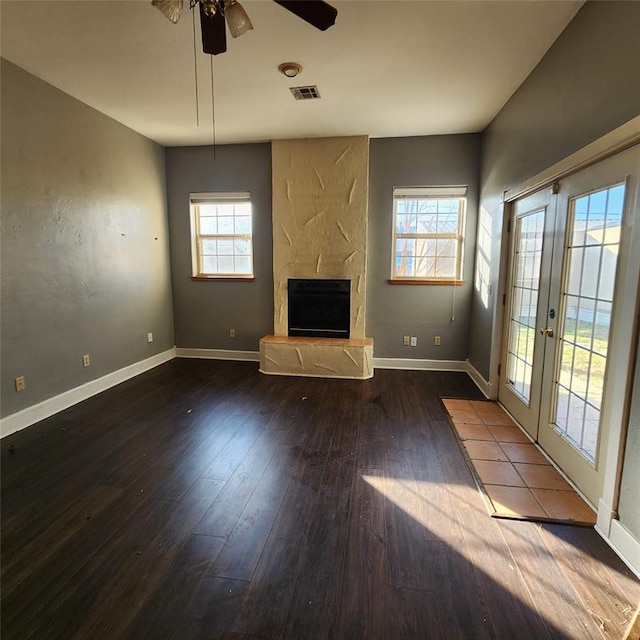 unfurnished living room featuring hardwood / wood-style flooring, ceiling fan, a large fireplace, and french doors