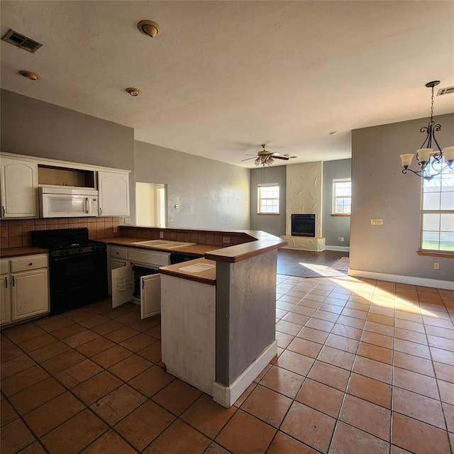 kitchen with black range oven, a high end fireplace, dark tile patterned flooring, decorative light fixtures, and ceiling fan with notable chandelier