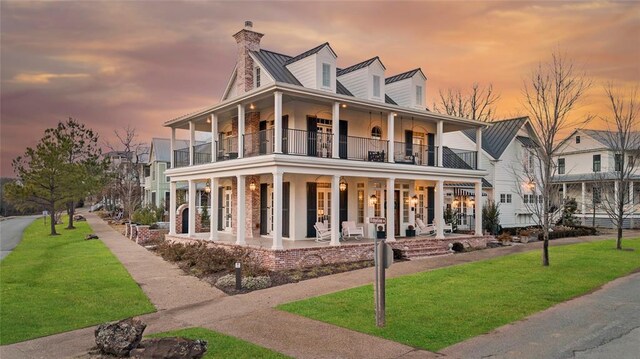 view of front of property featuring a balcony, a chimney, metal roof, a porch, and a front yard