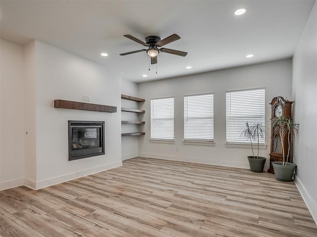 unfurnished living room featuring built in shelves, light hardwood / wood-style floors, and ceiling fan