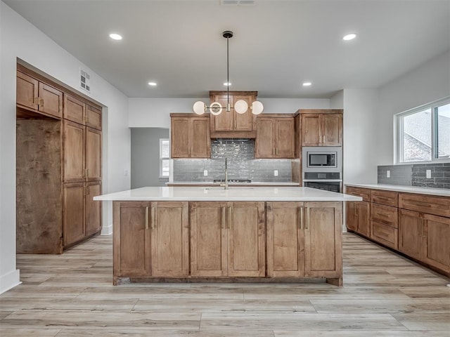 kitchen with a wealth of natural light, pendant lighting, an island with sink, and stainless steel appliances