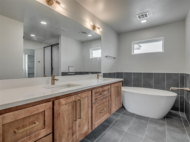 bathroom with tile patterned floors, a bathtub, tile walls, and vanity