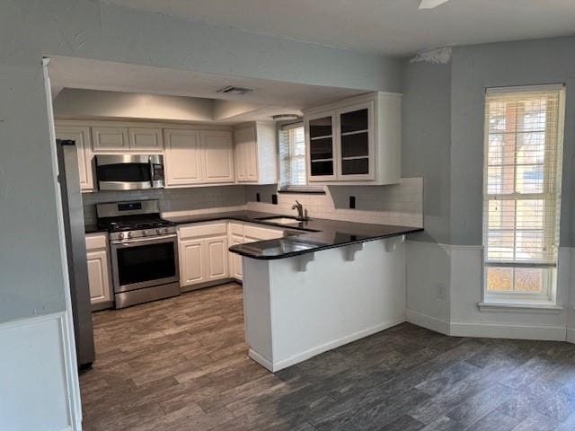 kitchen with dark countertops, dark wood-type flooring, a peninsula, stainless steel appliances, and a sink