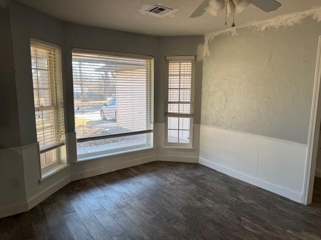 empty room featuring dark wood-style flooring, a wainscoted wall, ceiling fan, and visible vents