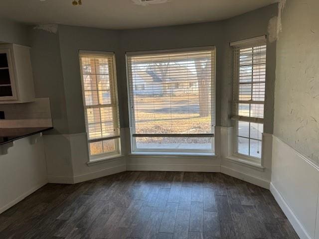 unfurnished dining area with baseboards, dark wood-style flooring, and a wealth of natural light