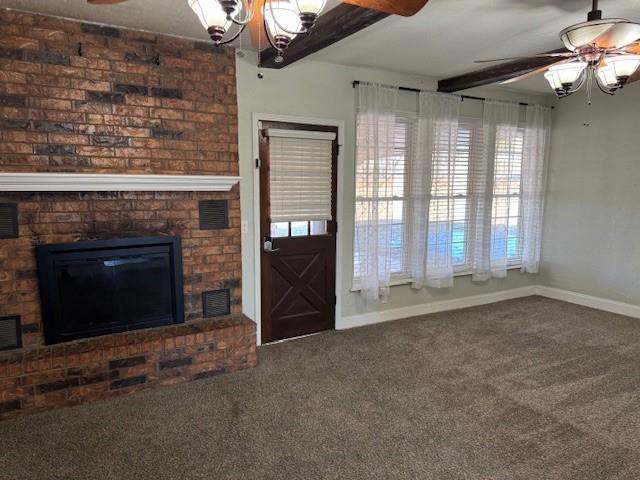 unfurnished living room featuring baseboards, visible vents, beamed ceiling, carpet, and a brick fireplace