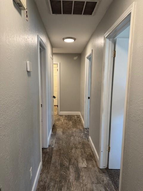 hallway with dark wood-style floors, baseboards, visible vents, and a textured wall