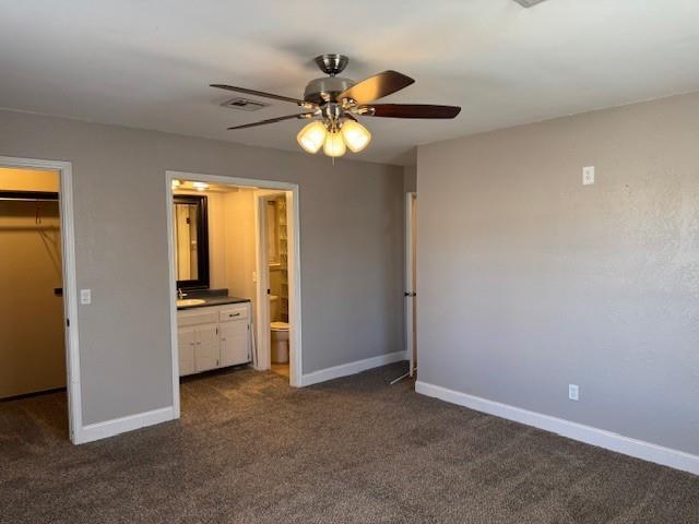 unfurnished bedroom with a walk in closet, baseboards, visible vents, and dark colored carpet