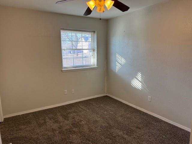 empty room featuring a ceiling fan, dark carpet, and baseboards