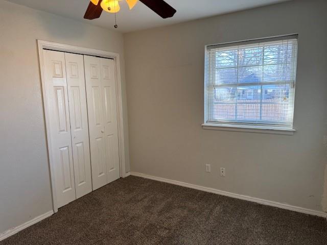 unfurnished bedroom featuring a ceiling fan, a closet, dark carpet, and baseboards